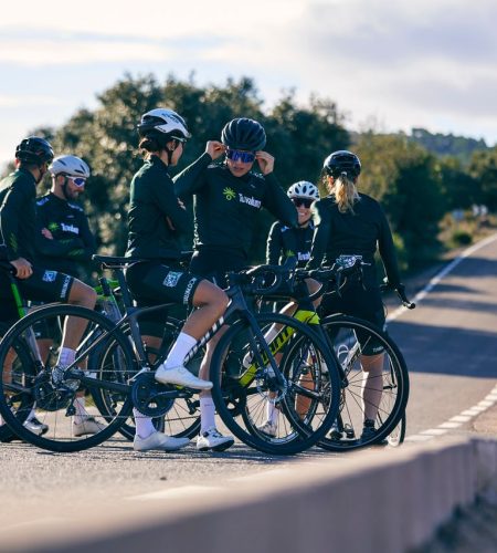 Cyclists wearing helmets and sportswear take a break on a rural road in daylight.